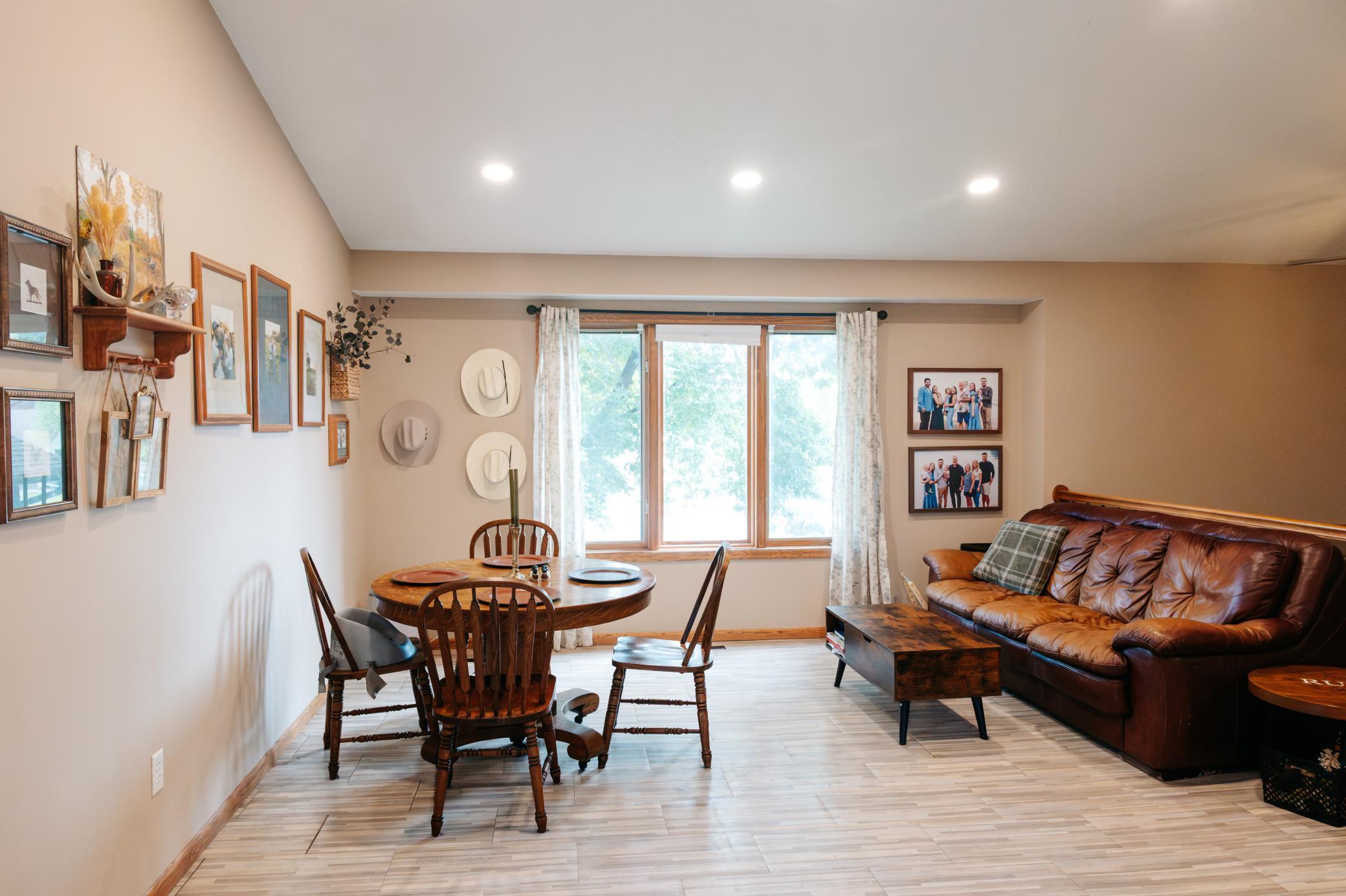 Living and dining area with a round wooden table, brown leather sofa, and large curtained window.