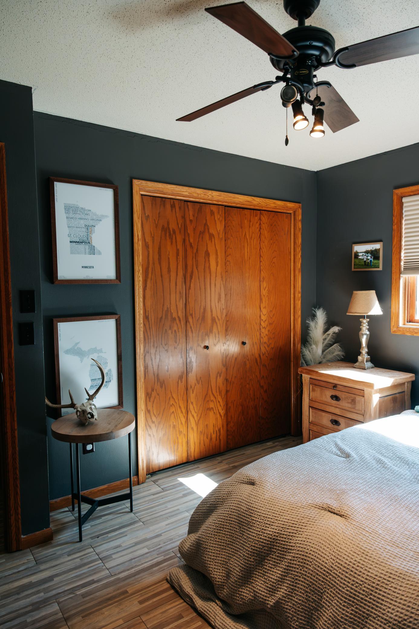 Bedroom with dark teal walls, wooden closet doors, and a ceiling fan above the bed.