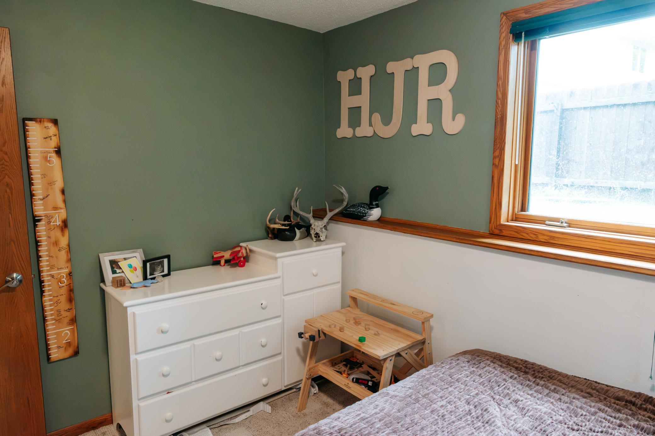 Child's bedroom with green walls, a white dresser, wooden toy workbench, and large HJR initials.