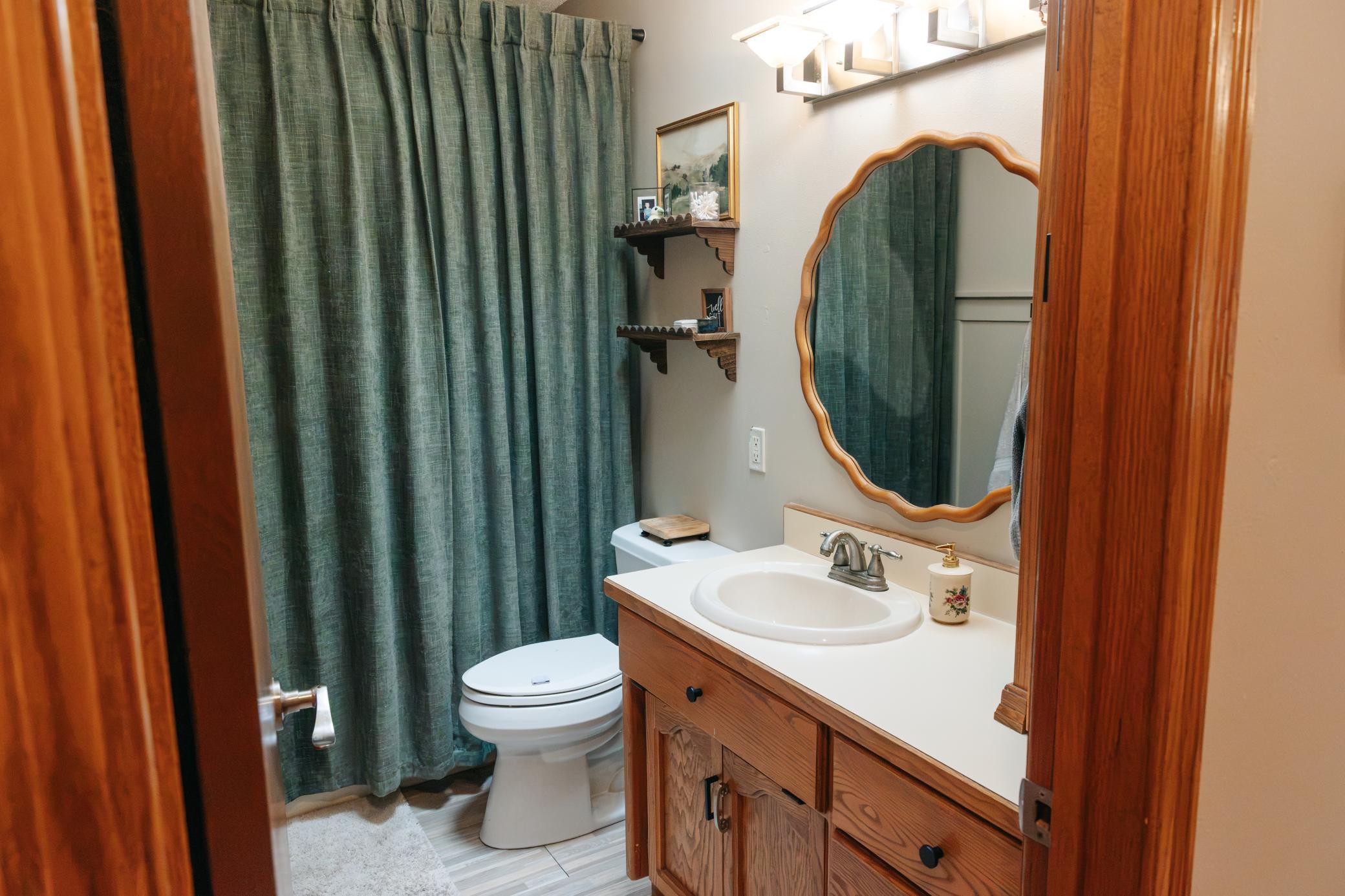 Bathroom with a wood vanity, scalloped mirror, and dark green shower curtain.