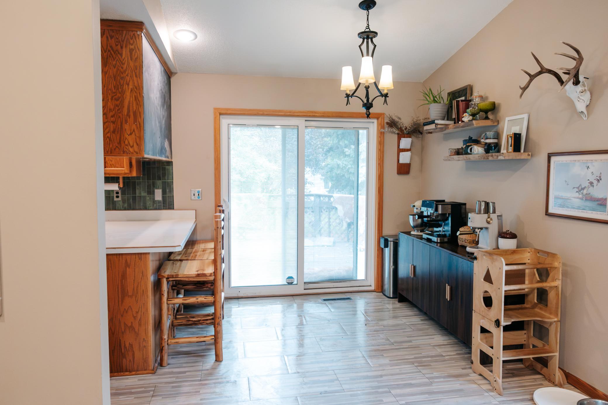Kitchen with wood cabinetry, counter stools, coffee station, and sliding glass door.