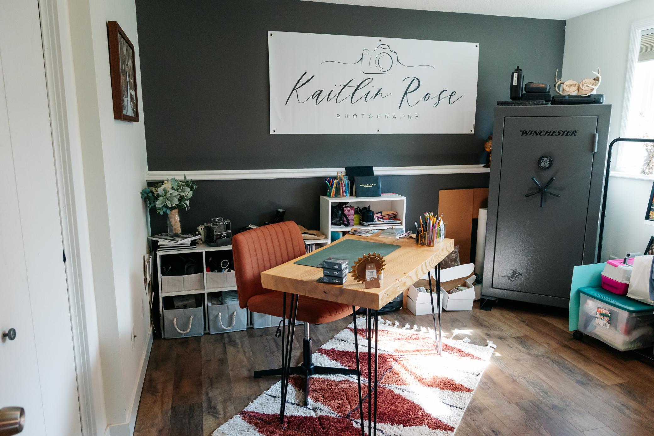 Furnished home office with a wooden desk, rust-colored chair, and large photography sign above a tall safe.