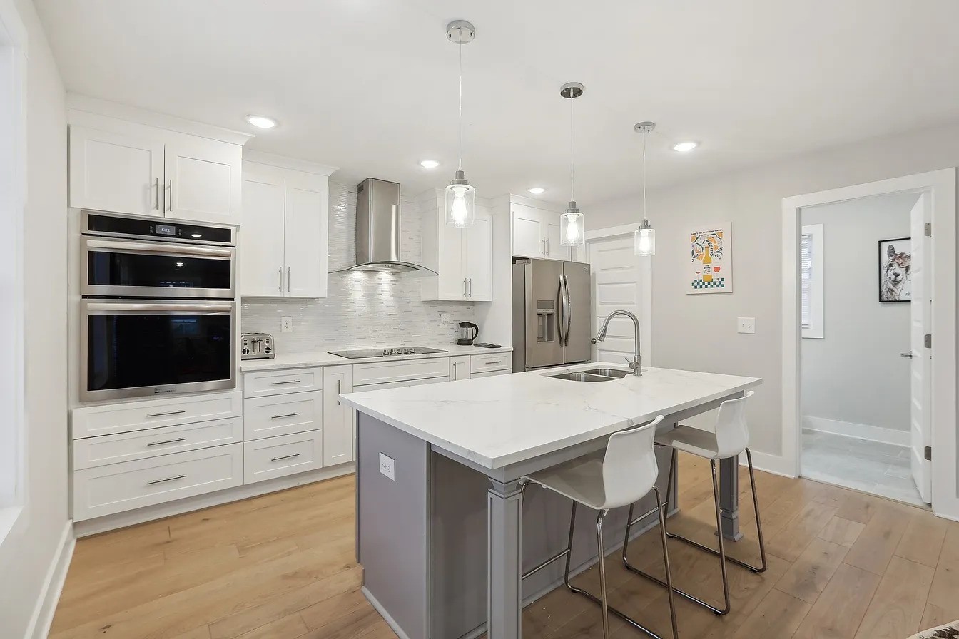 Modern white kitchen with stainless steel appliances and a large island with sink and seating.
