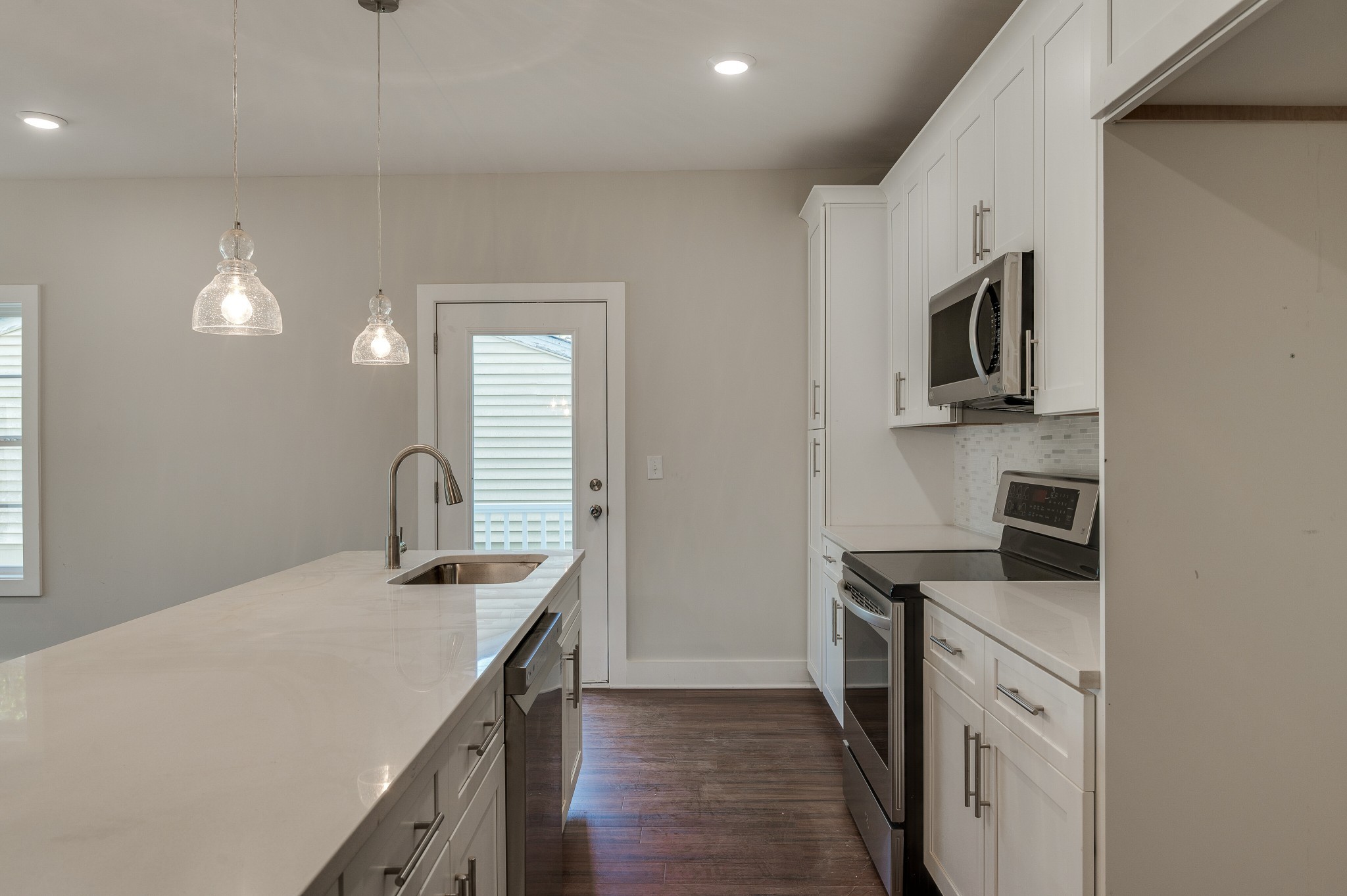 Modern kitchen with a quartz island and sink, white cabinetry, and stainless steel appliances.