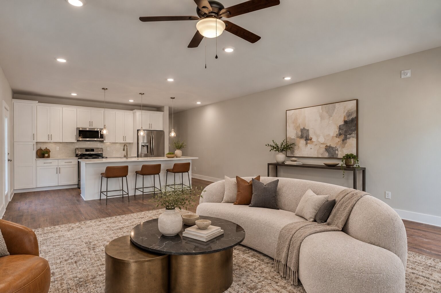 Open-plan living room and kitchen with a curved cream sofa, white cabinetry, and island seating.