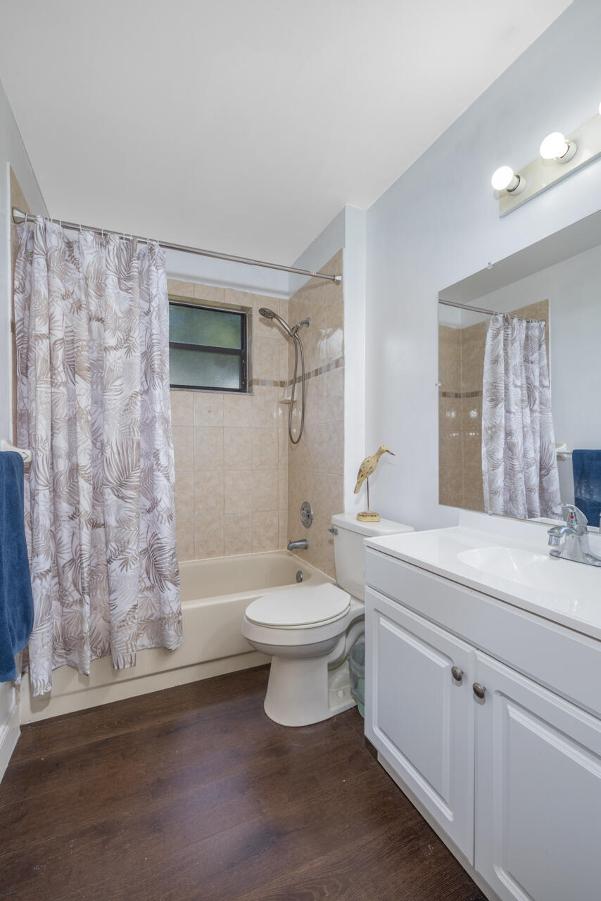 Bathroom with a white vanity, toilet, and bathtub behind a patterned shower curtain.