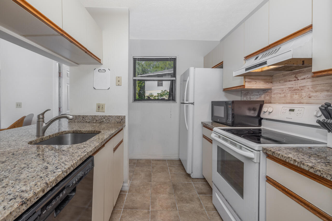 Kitchen with granite counters, wood-trim cabinets, white appliances, and a window.