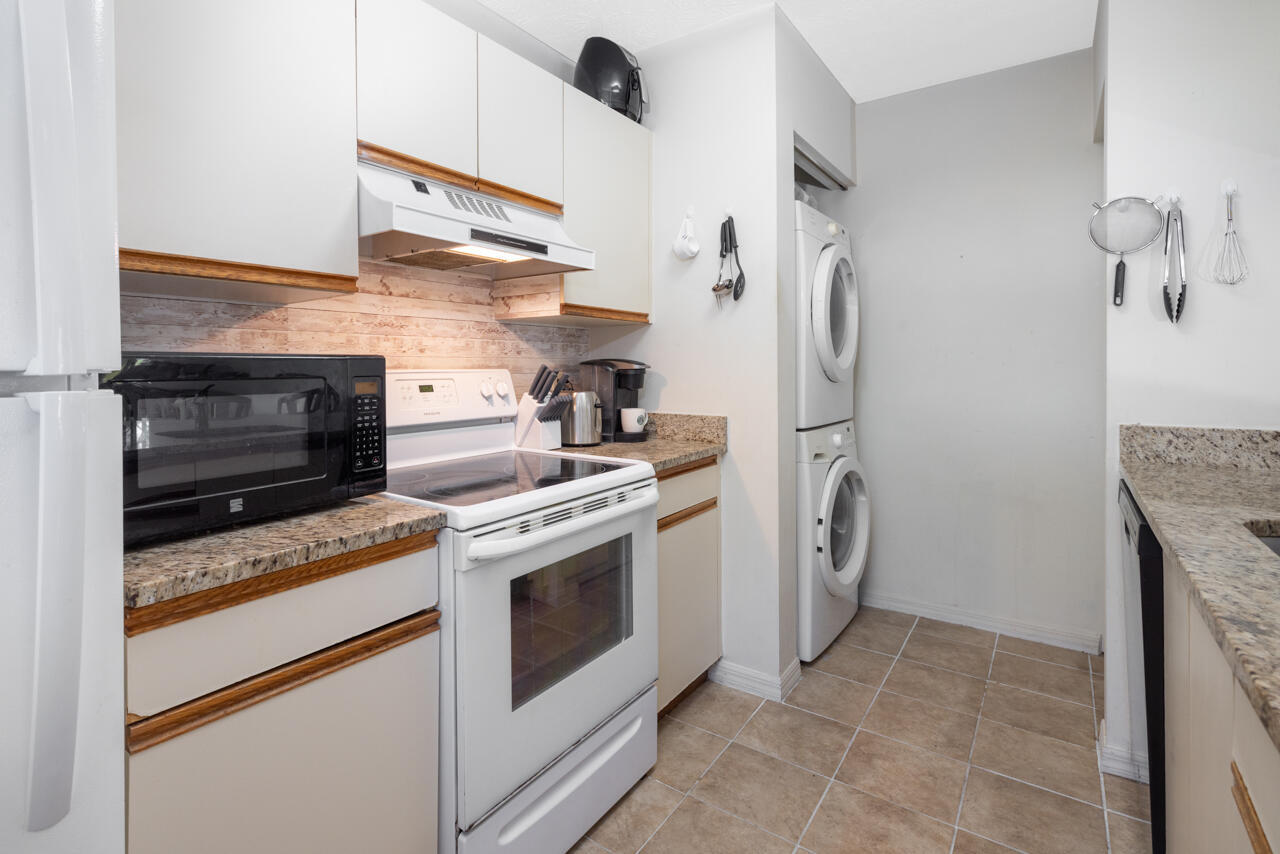 Kitchen with white wood-trimmed cabinets, granite counters, a white range, and stacked washer and dryer.