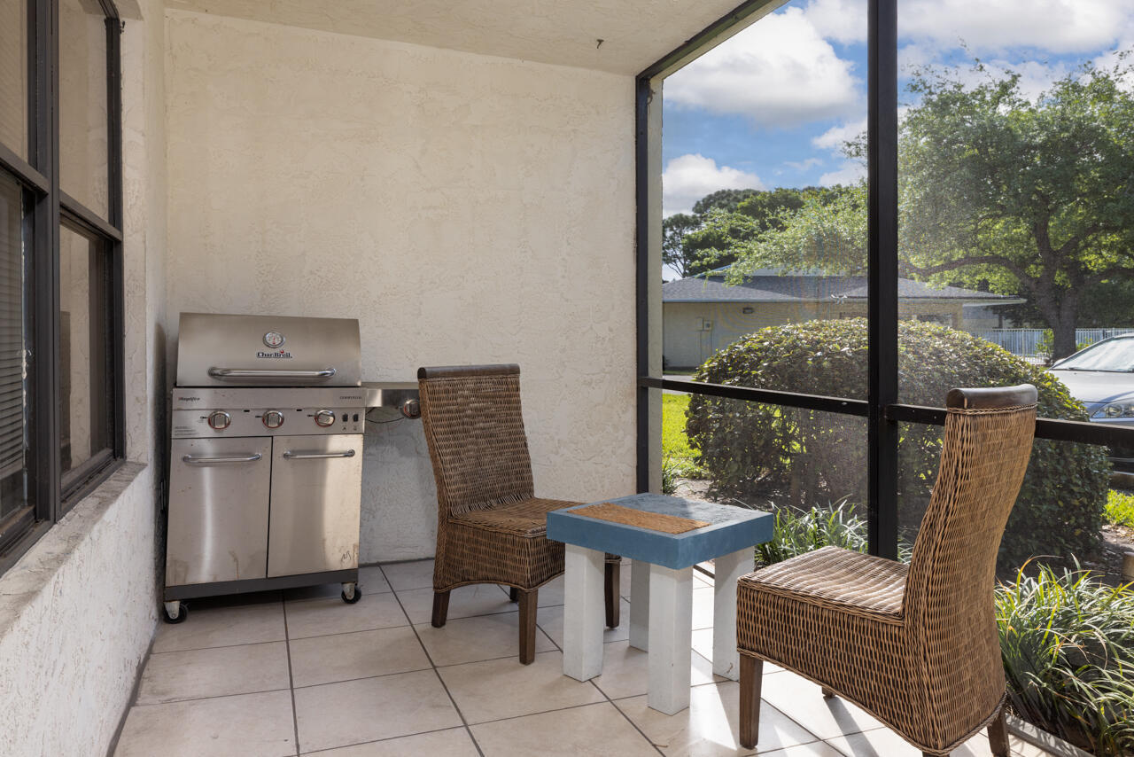 Screened patio with a stainless steel grill, wicker seating, and a small table.