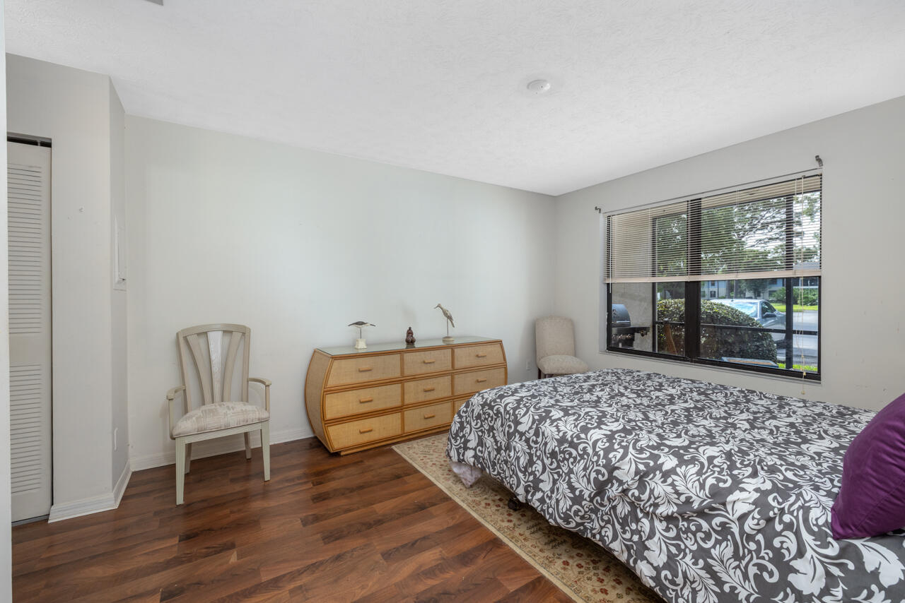 Bedroom with a floral bedspread, curved wooden dresser, and wide window with blinds.