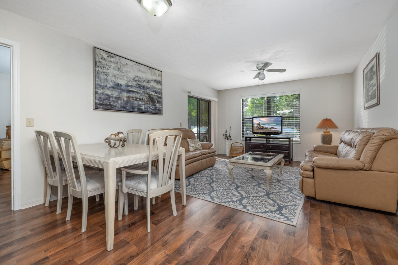 Living and dining room with tan leather sofas, a white dining set, patterned rug, and dark hardwood floors.
