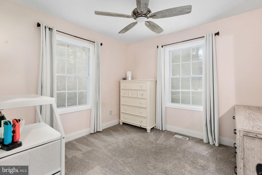 Bedroom with two curtained windows, gray carpet, and a ceiling fan.
