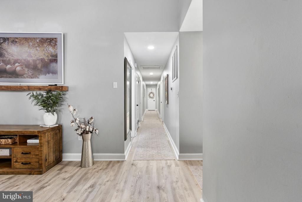Furnished hallway with light wood floors, a long runner, and a wooden console beside the entry.