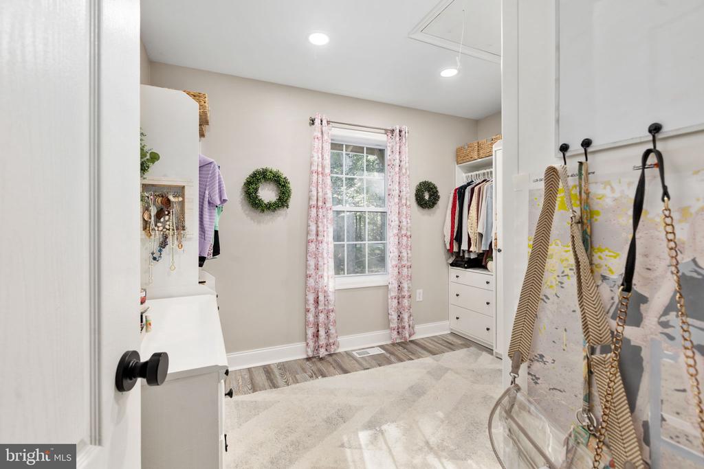 Walk-in closet with built-in drawers, clothing racks, and a window framed by pink floral curtains.