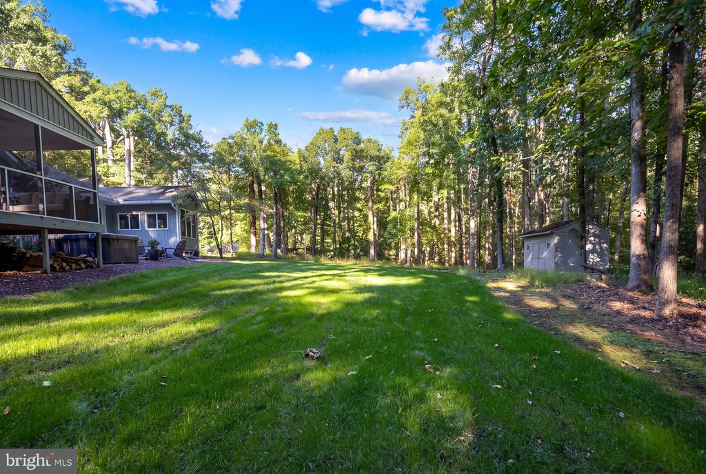 Wooded backyard with a broad lawn, screened deck, and small shed.