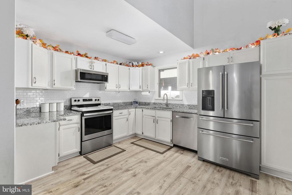 Kitchen with white cabinets, stainless steel appliances, subway-tile backsplash, and light wood-look flooring.