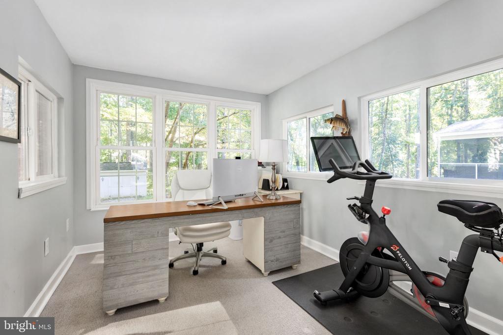 Home office with a gray desk, large windows, and a Peloton exercise bike.