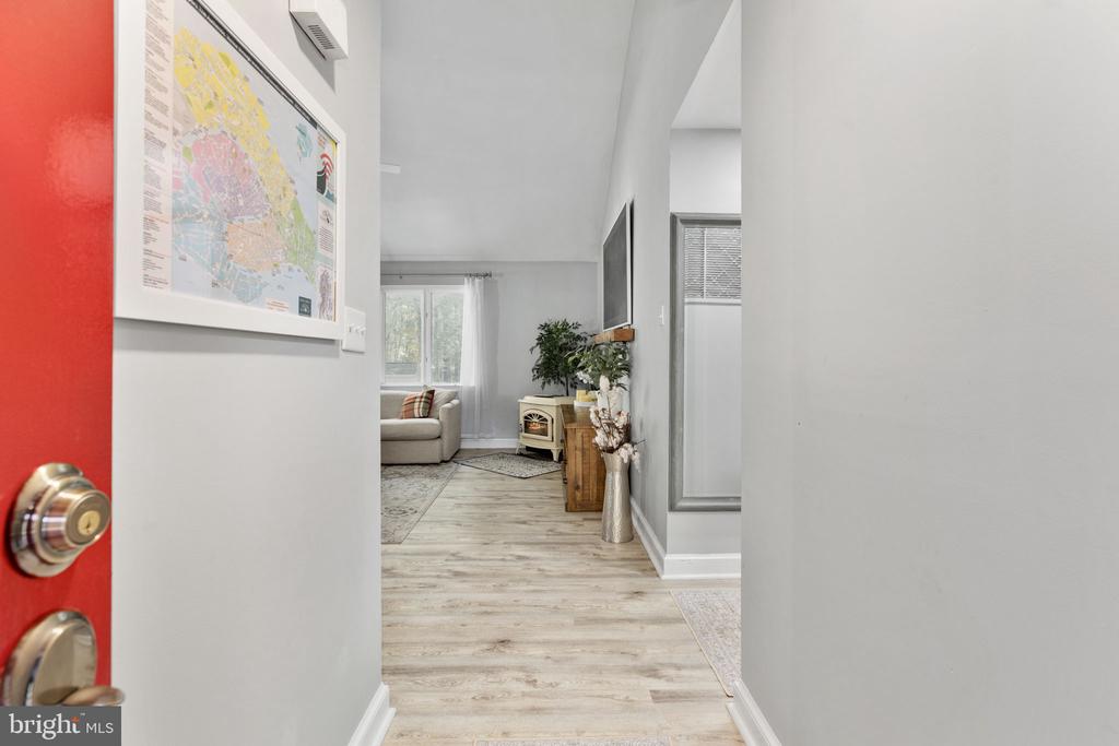 Entry hall with light wood flooring leads to a furnished living room beyond the open red door.