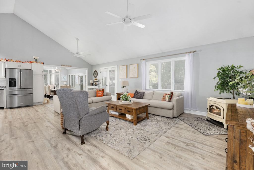 Furnished open-plan living room with a vaulted ceiling, gray sectional, large windows, and adjoining kitchen.