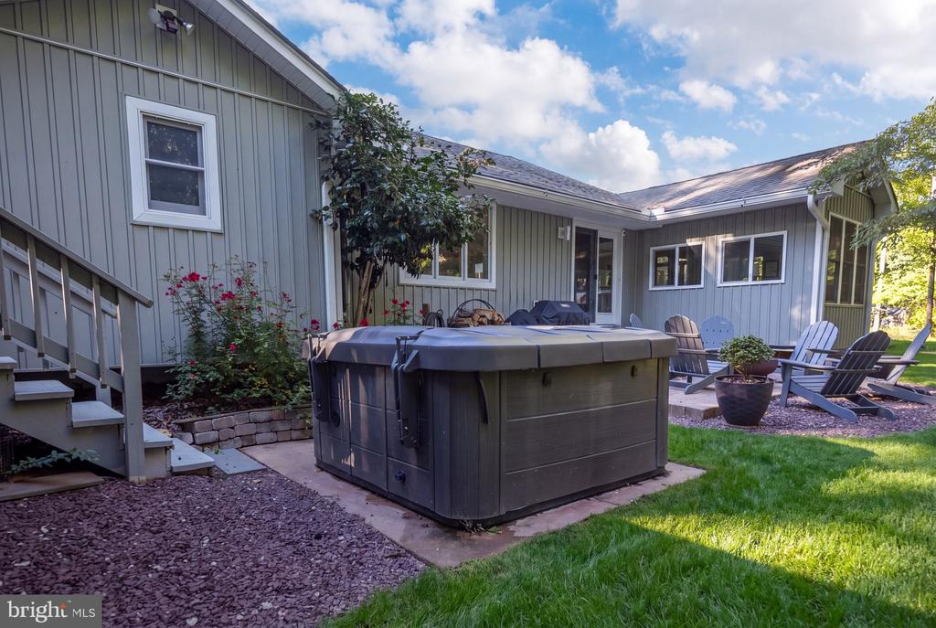 Gray-sided home with a large hot tub and Adirondack chairs on the backyard patio.