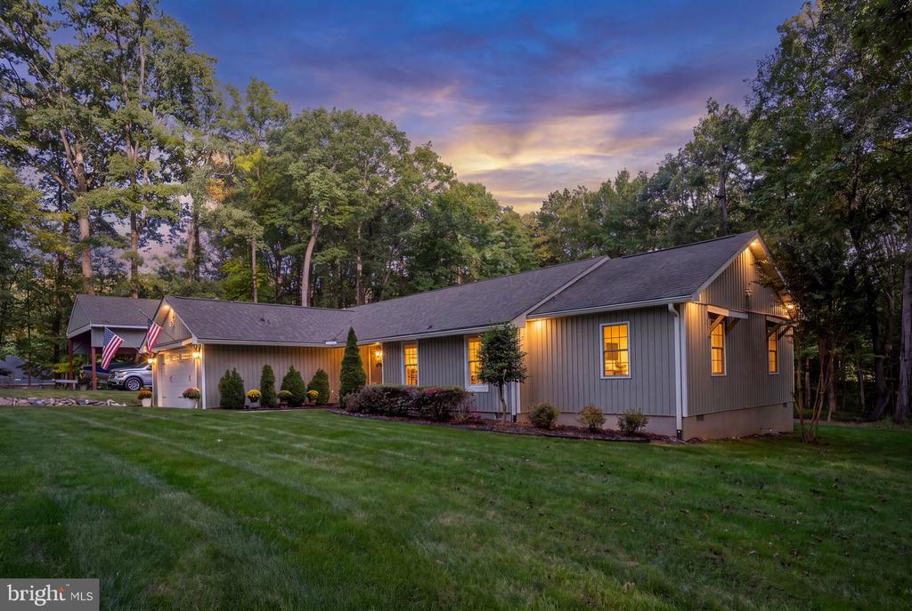 Gray single-story home with glowing windows and a broad lawn at dusk.