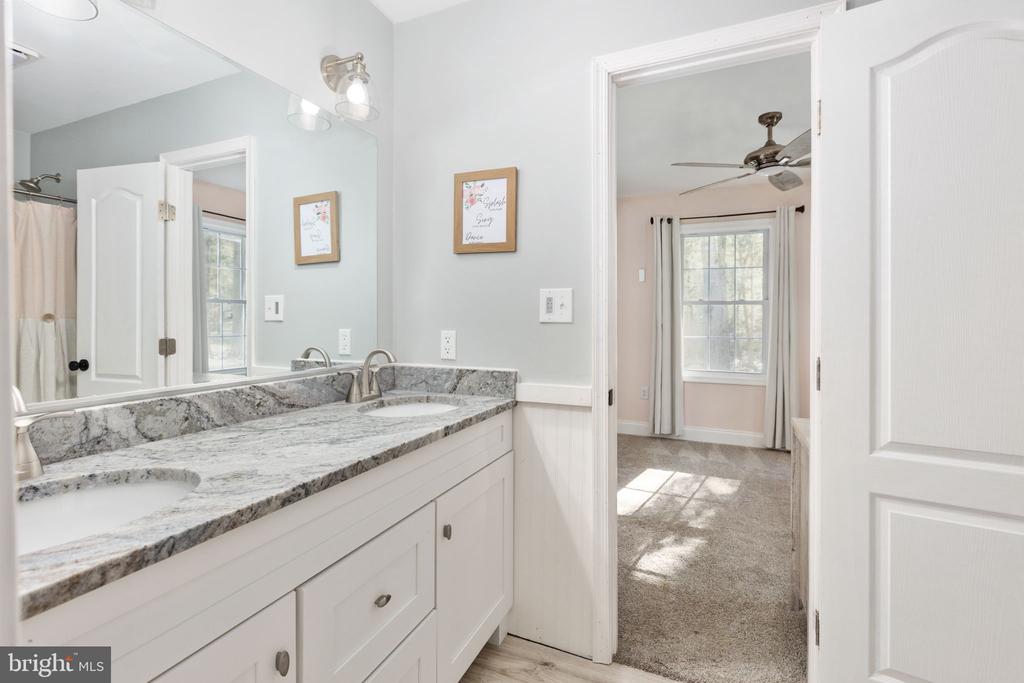 Bathroom vanity with granite countertop and mirror, looking through an open doorway into a bedroom.