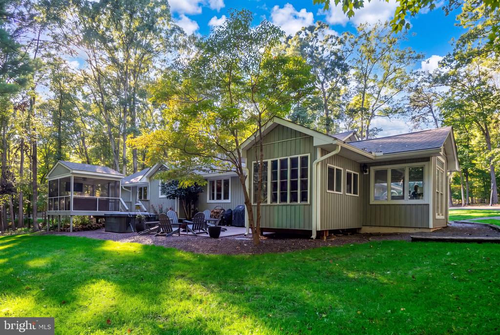 Green-sided home with a screened porch, large windows, and patio seating beneath mature trees.