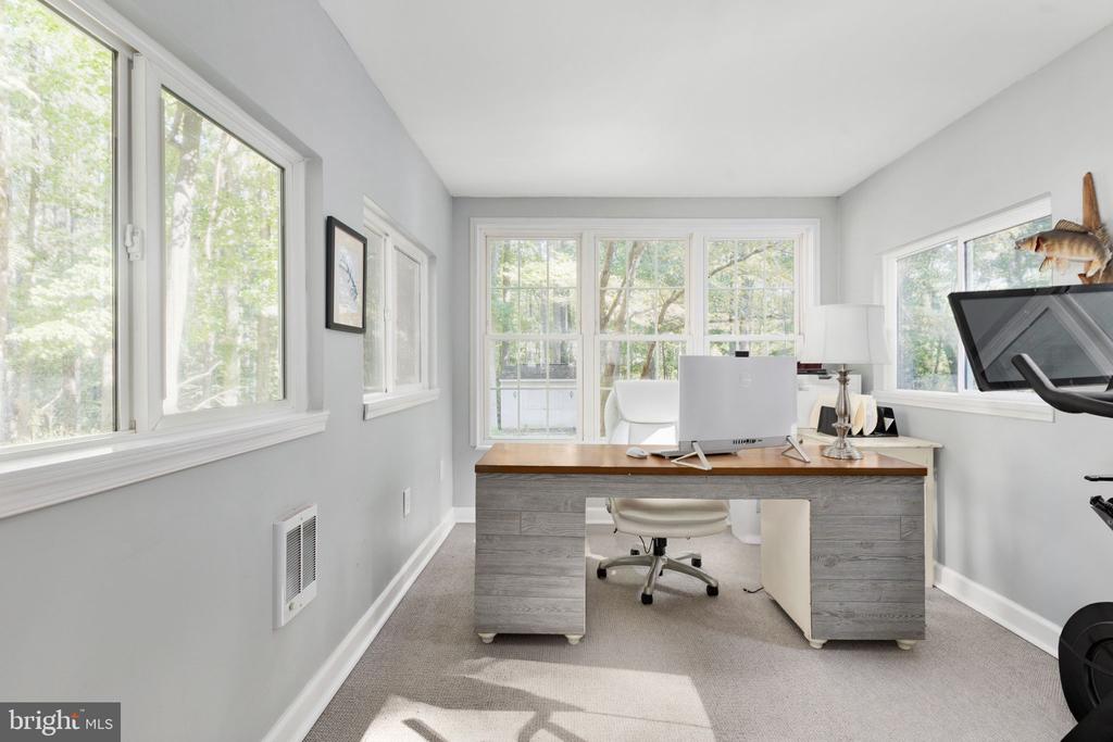 Home office with a gray desk and large windows overlooking trees.