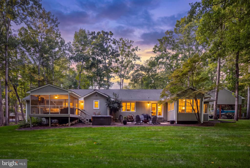 Gray single-story home with a screened porch, hot tub, and outdoor seating at dusk.