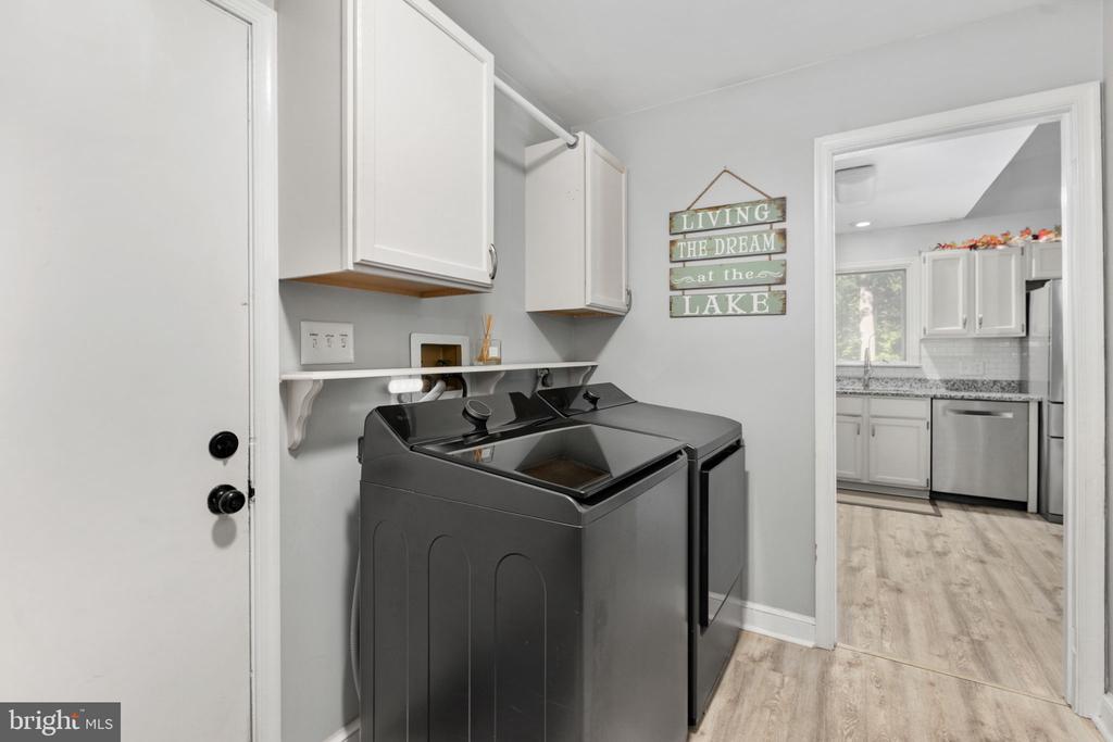 Laundry room with dark washer and dryer, white cabinets, and a doorway to the kitchen.