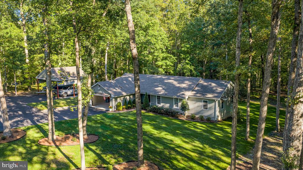 Aerial view of a single-story home among mature trees, with a detached carport and landscaped lawn.
