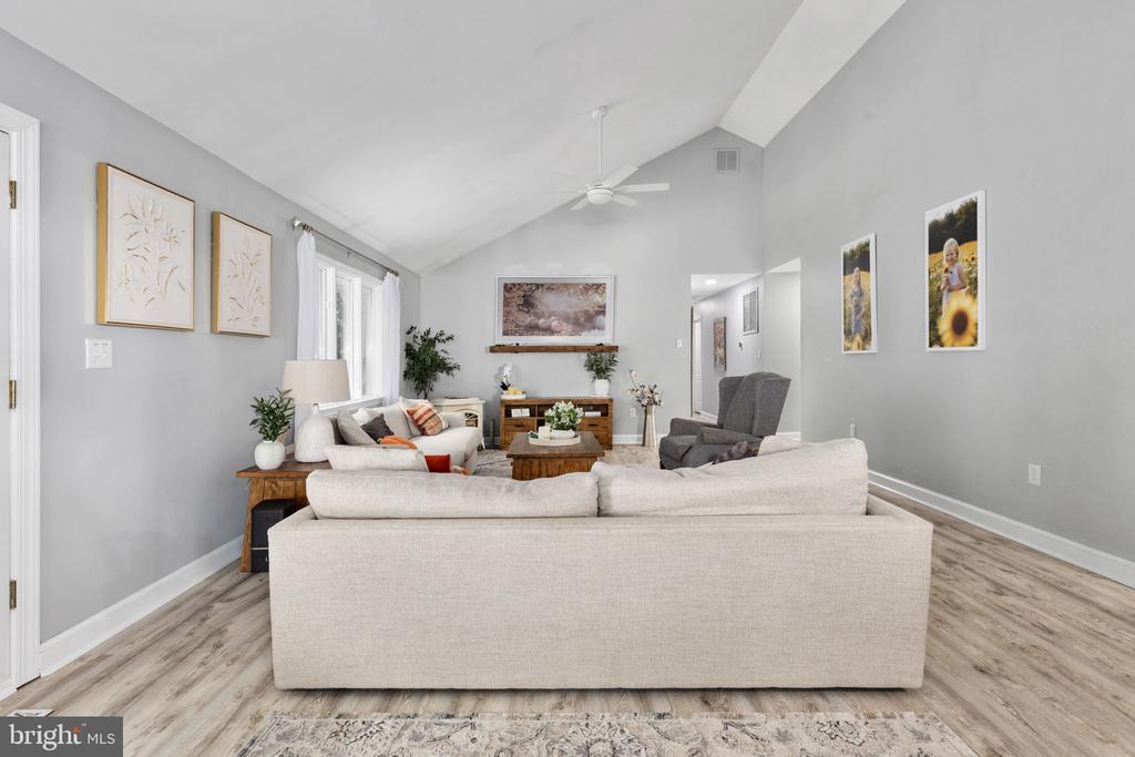 Living room with a vaulted ceiling, white sofas, gray walls, and light wood flooring.