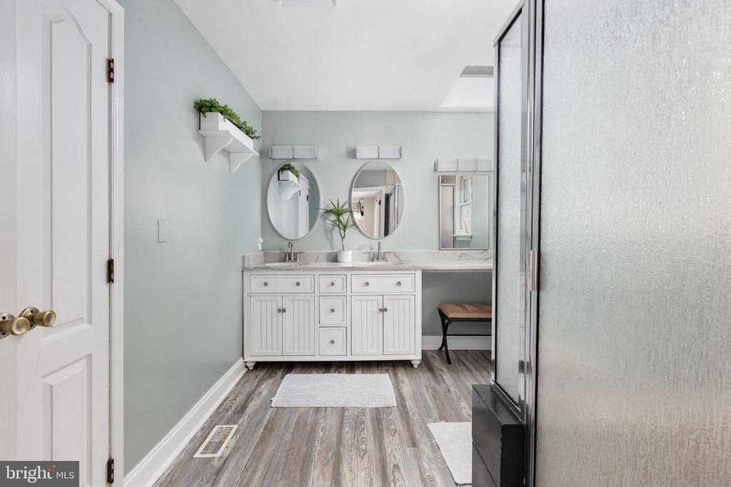 Bathroom with a white double vanity, oval mirrors, and a glass shower enclosure.