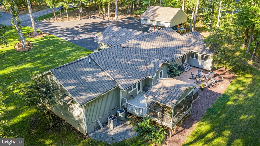 Aerial view of a tree-surrounded home with a screened porch, patio seating, and detached carport.