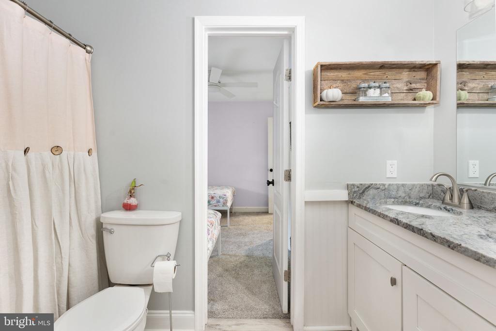 Bathroom with a white vanity, marble-pattern countertop, and doorway to a carpeted bedroom.