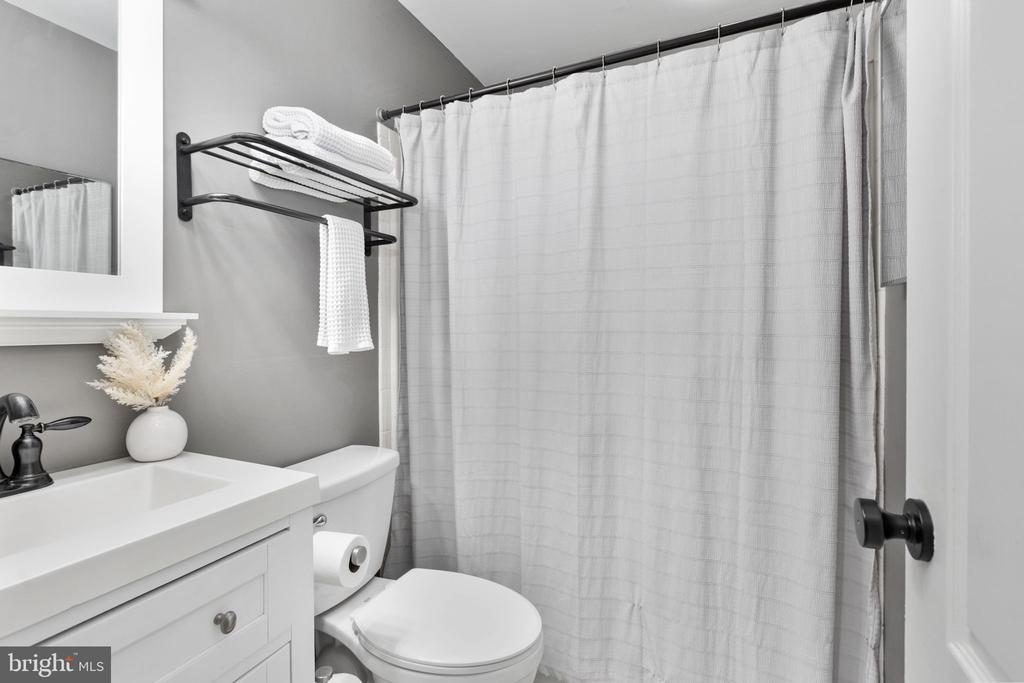 Bathroom with a white vanity, toilet, and tub-shower behind a curtain.