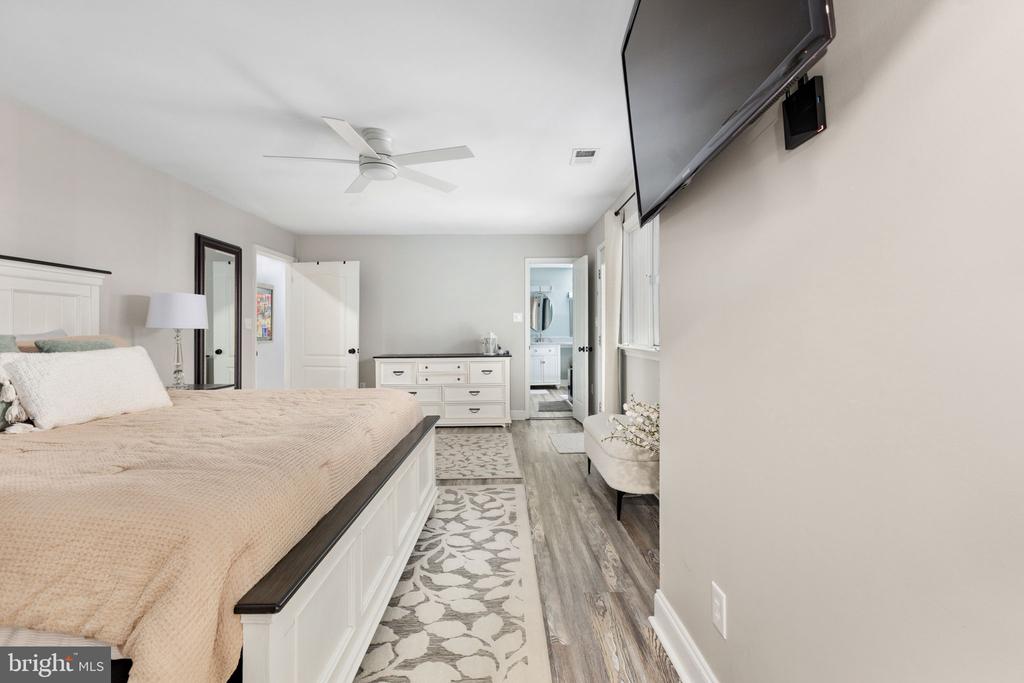 Furnished bedroom with a large bed, ceiling fan, dresser, and bathroom doorway.