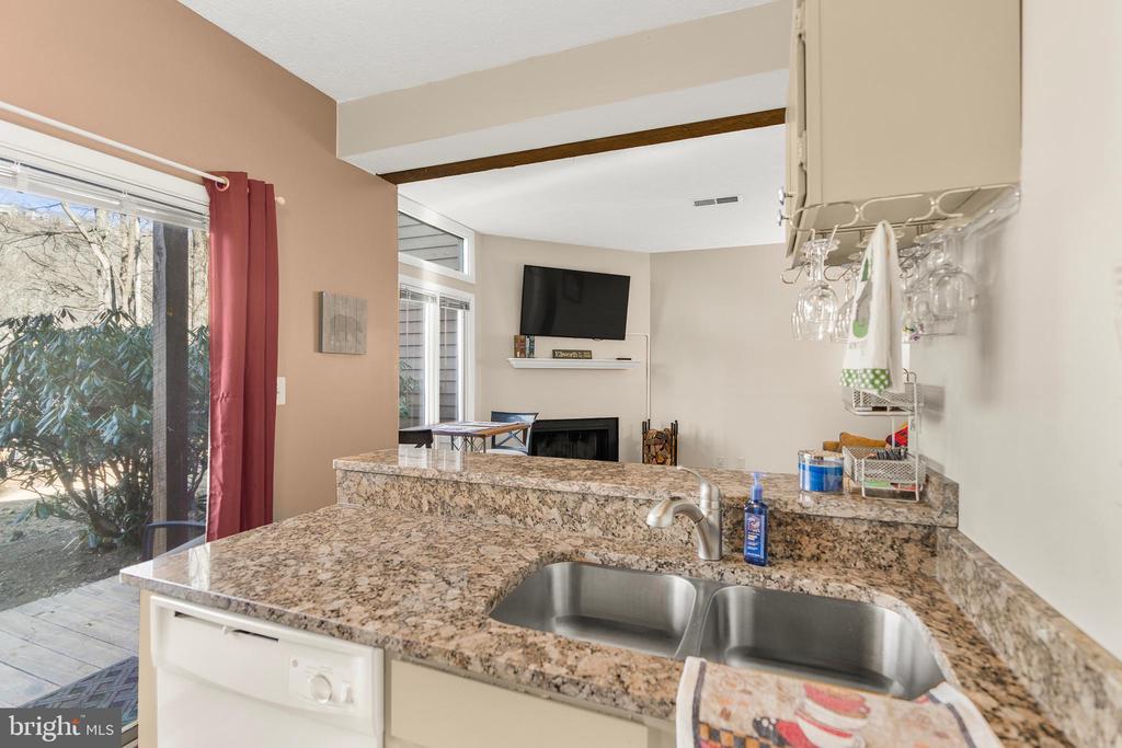 Kitchen with granite counters and double sink overlooking a living room with a fireplace.