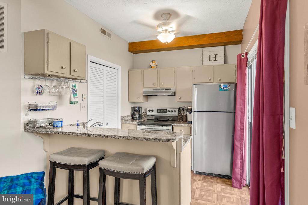 Kitchen with a granite breakfast bar, two stools, stainless steel appliances, and magenta curtains.