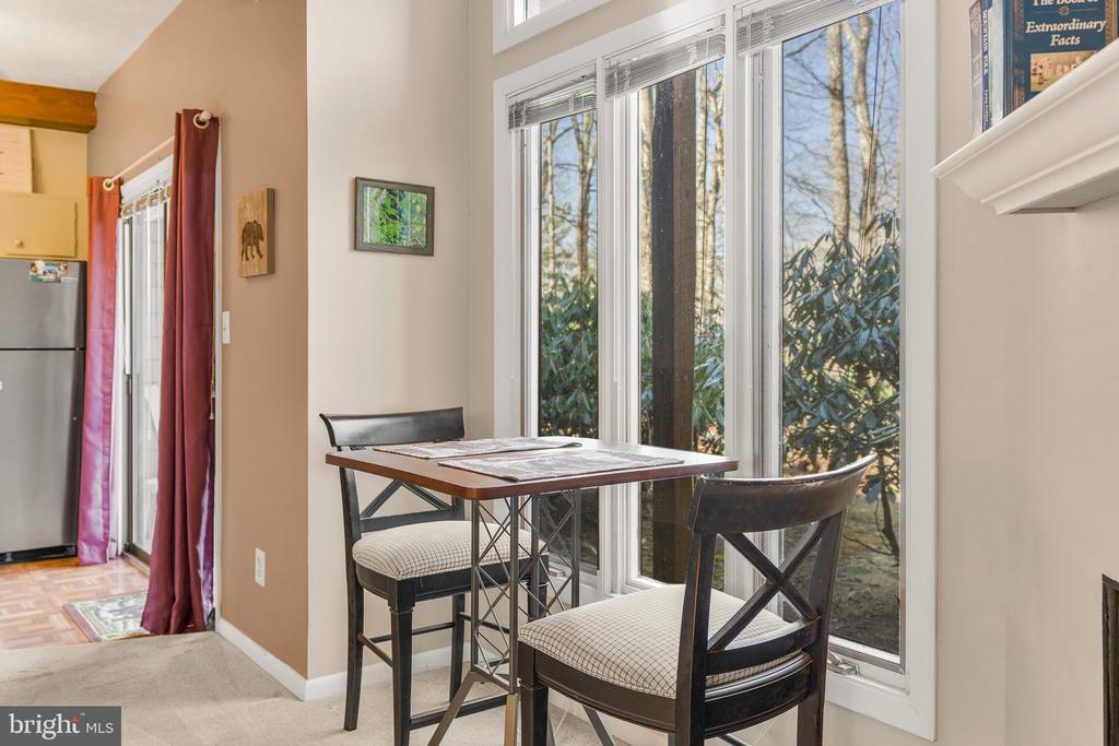 Dining area with a small table and two chairs beside tall windows overlooking trees.