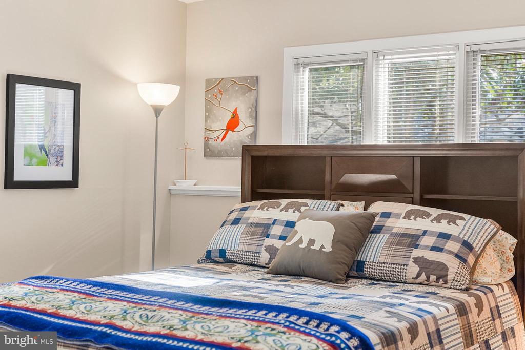 Bedroom with plaid bedding, bear-print pillows, a dark wood headboard, and wide windows with blinds.