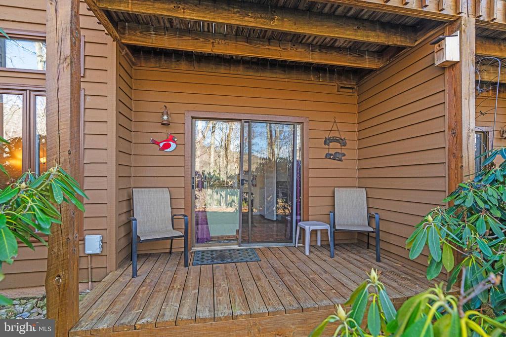 Covered wooden deck with two chairs and a sliding glass door.