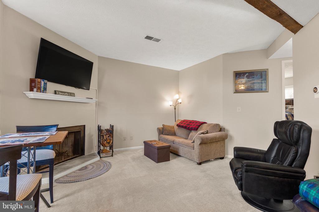 Living room with vaulted ceiling, fireplace, wall-mounted television, and beige seating.