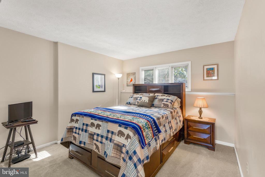 Bedroom with a wooden bed, patterned quilt, window blinds, and television.
