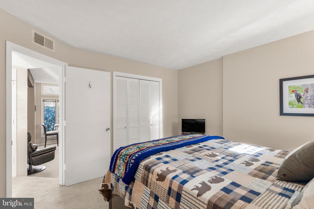 Bedroom with a patterned quilt-covered bed, louvered closet, and doorway to a sitting area.