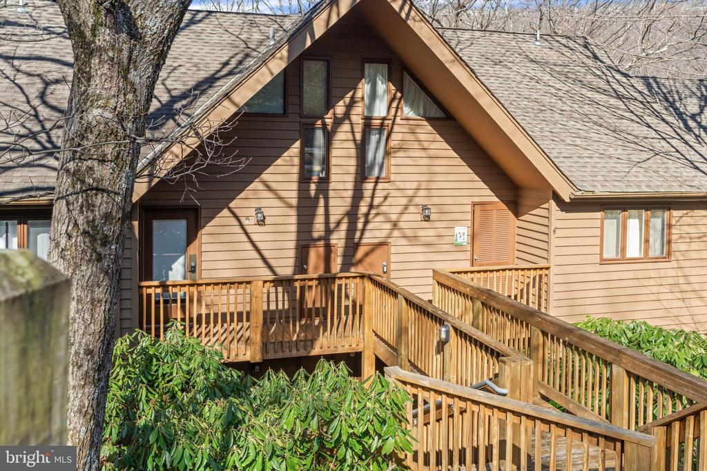 Brown-sided house with a steep gabled roof and elevated wooden deck with ramp.