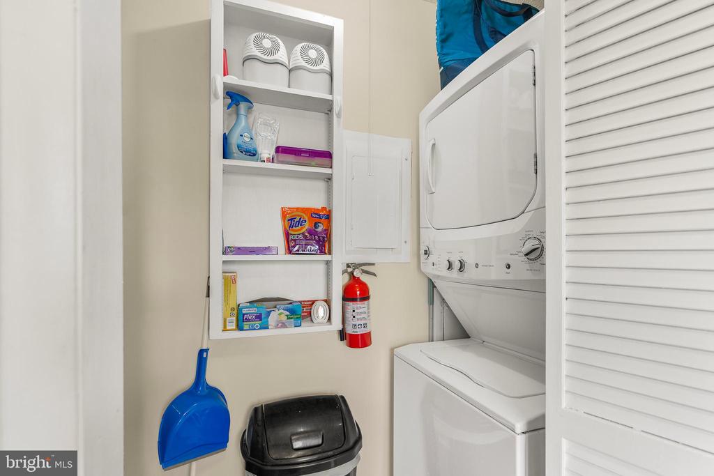 Laundry room with stacked washer and dryer beside shelves stocked with cleaning supplies.
