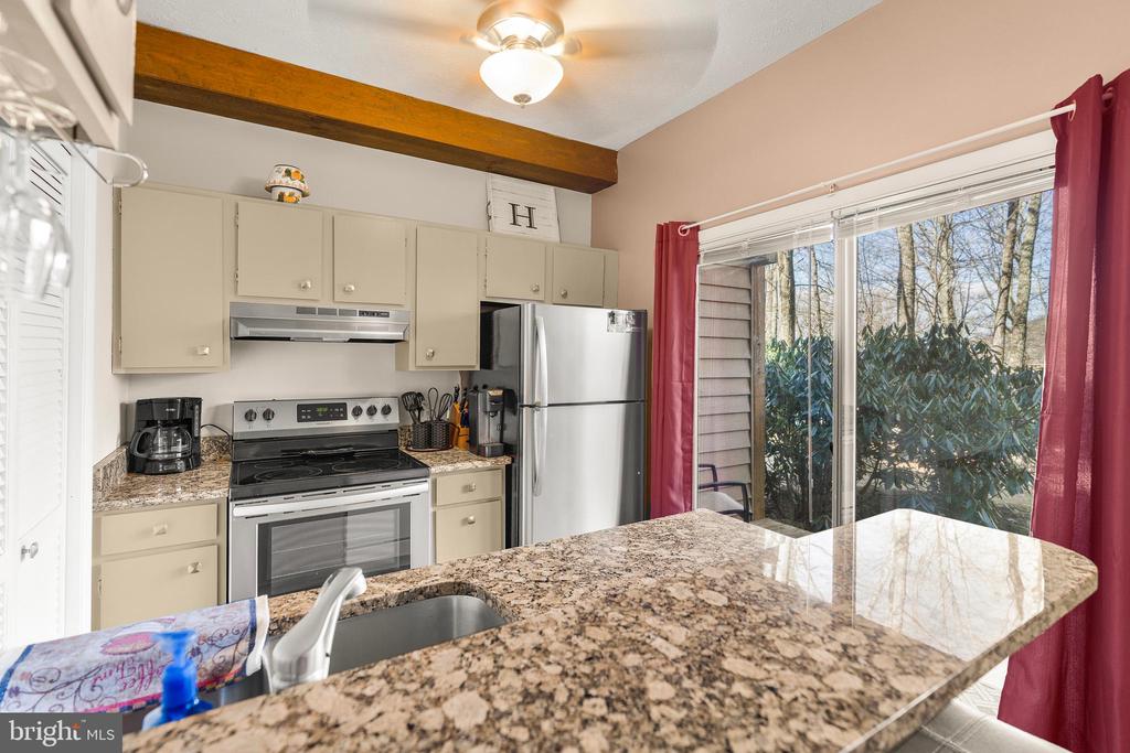 Kitchen with granite breakfast bar, cream cabinets, stainless steel appliances, and sliding doors to a wooded yard.