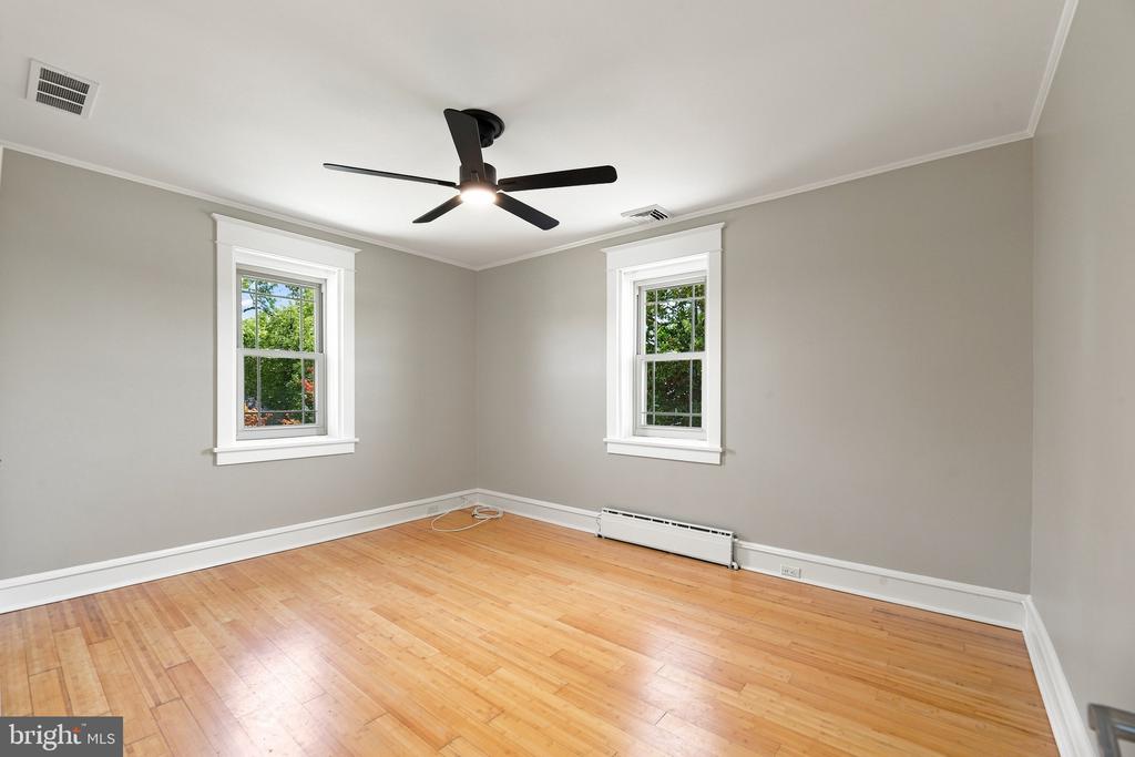 Empty room with hardwood floors, two windows, and a dark ceiling fan.