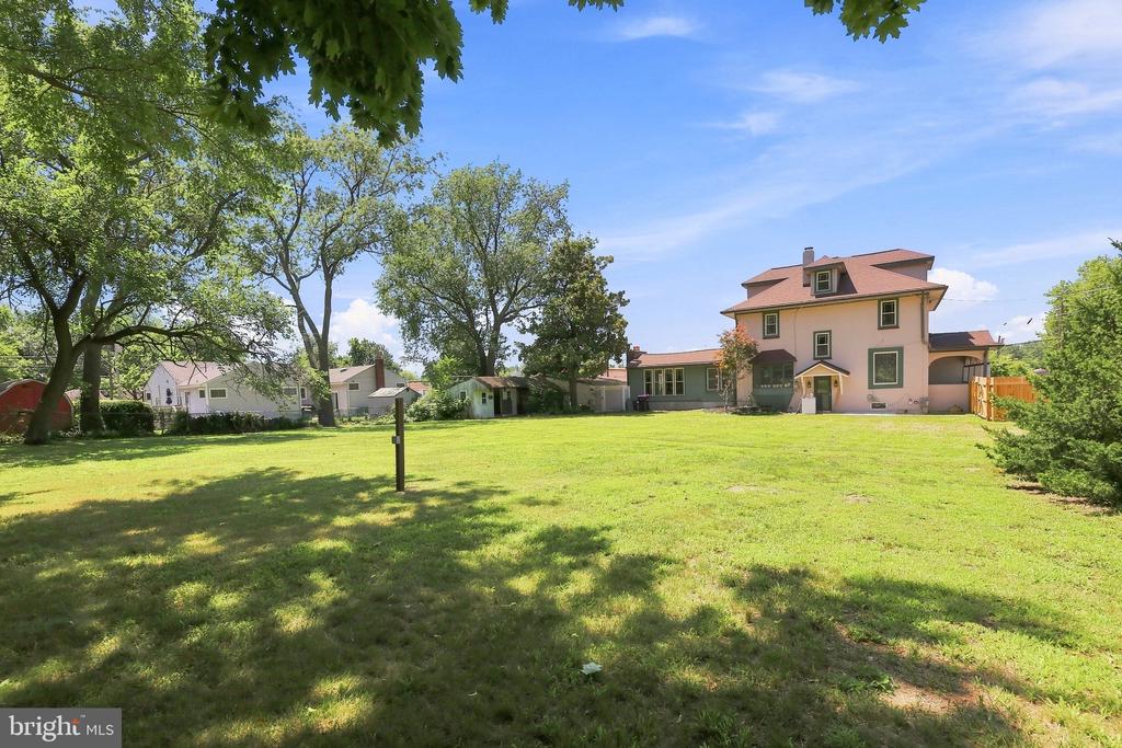 A broad grassy backyard leads to a two-story house, with mature trees shading the lawn.